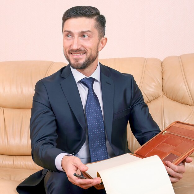 Uomo d'affari di successo impegnato in documenti aziendali seduto su un divano in pelle