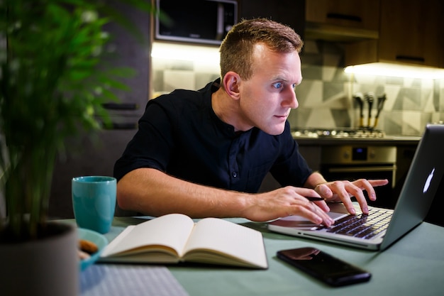 Uomo d'affari di successo seduto a casa al tavolo, guarda lo schermo del laptop, si sente orgoglioso del lavoro svolto, l'uomo sereno lavora, lavora a casa