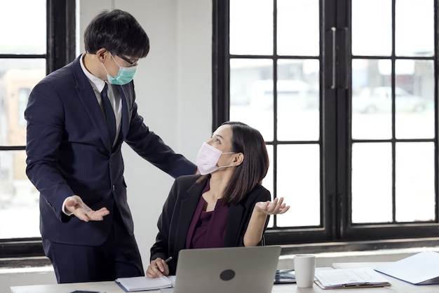 Uomo d'affari e bella donna d'affari seduti alla scrivania nell'ufficio di coworking con maschera facciale a causa del Covid-19