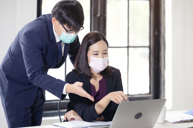 Uomo d'affari e bella donna d'affari seduti alla scrivania nell'ufficio di coworking con maschera facciale a causa del Covid-19