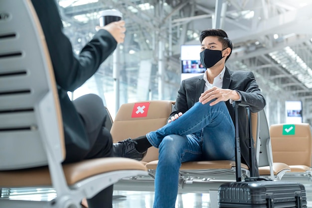 Uomo d'affari e donna con protezione della maschera facciale incontro informale con sedile di distanza sociale al terminal dell'aeroporto nuovo concetto di business lifestyle