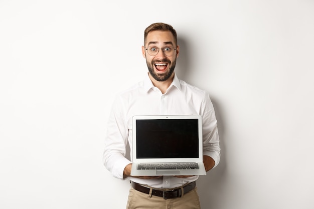 Uomo d'affari eccitato che mostra qualcosa sullo schermo del laptop, in piedi felice su sfondo bianco