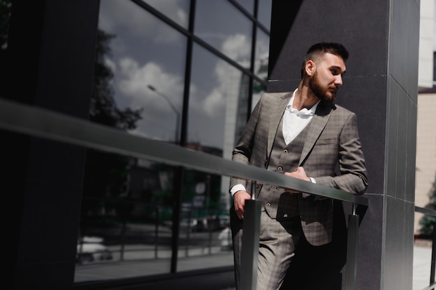 Uomo d'affari elegantemente vestito, uomo d'affari moderno. Fiducioso giovane uomo in tuta intera in piedi all'aperto con la costruzione in background