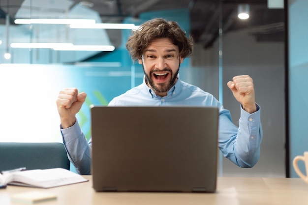 Uomo d'affari emozionante che usa il pc che celebra il successo agitando i pugni gridando sì