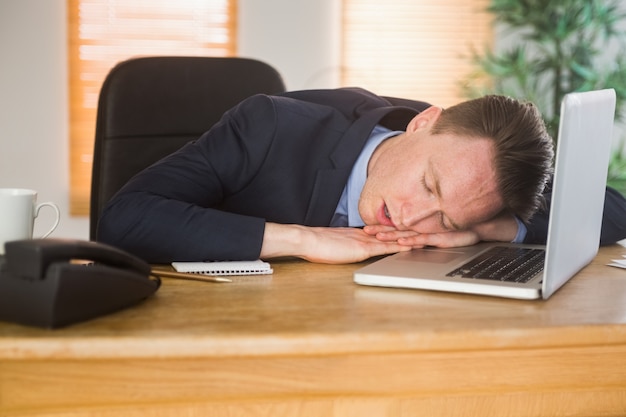 Uomo d&#39;affari esaurito che dorme sul suo computer portatile