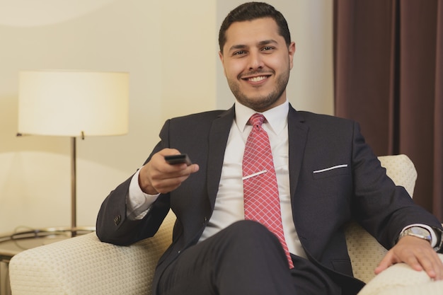 Uomo d'affari facendo uso del telecomando mentre si guarda la TV nella sua camera d'albergo