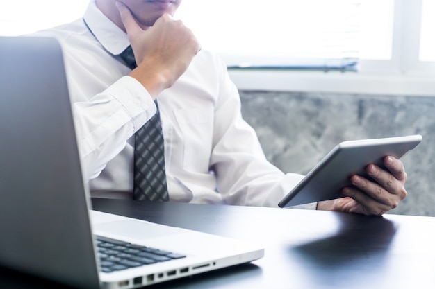 Uomo d&#39;affari facendo uso della compressa e del computer portatile sullo scrittorio