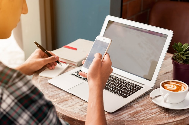 Uomo d'affari facendo uso dello smartphone e del computer portatile con una tazza di caffè che prende nota