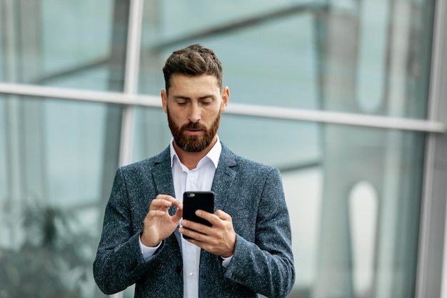 Uomo d'affari facendo uso dello smartphone e sorridendo all'aeroporto. Giovane uomo d'affari con il cellulare in aeroporto.