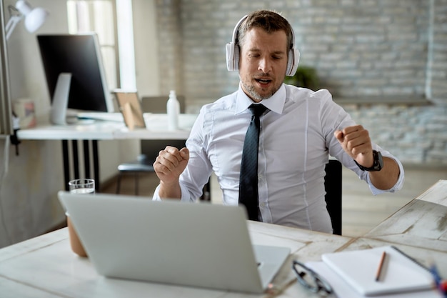 Uomo d'affari felice che ascolta musica e si diverte mentre si prende una pausa dal lavoro in ufficio