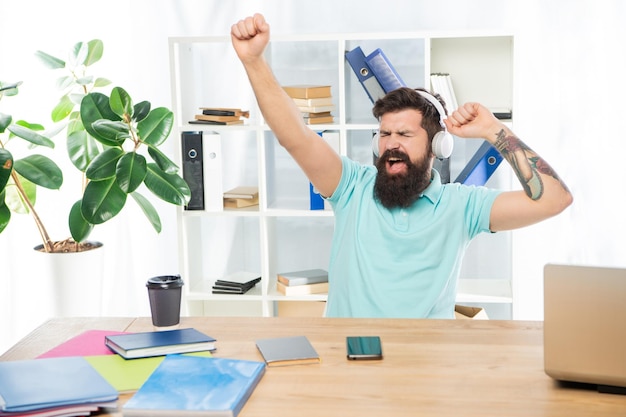 Uomo d'affari felice che fa gesto vincente ascoltando le cuffie nella musica d'ufficio