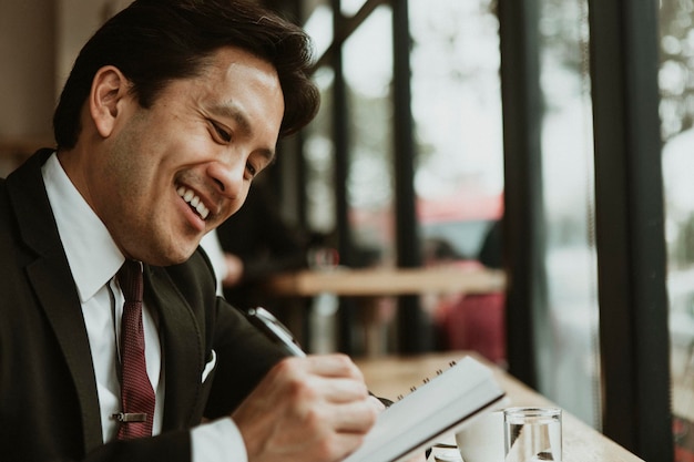 Uomo d'affari felice che scrive in un caffè