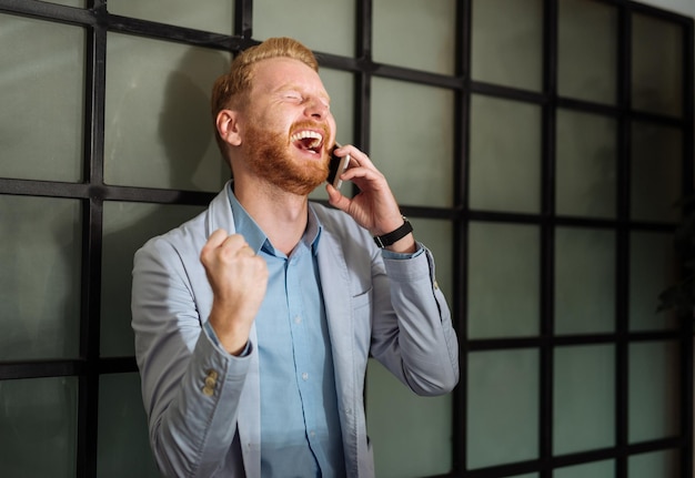 Uomo d'affari felice che sente grandi notizie al telefono.