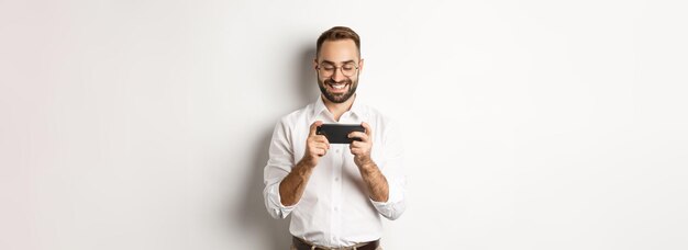 Uomo d'affari felice guardando video sul telefono cellulare in piedi su sfondo bianco