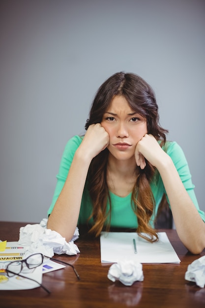 Uomo d'affari femminile frustrato che si siede con le palle di carta sgualcite