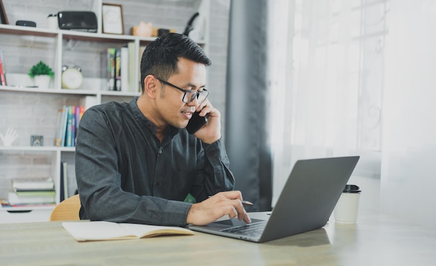 Uomo d'affari freelance che chiama uno smartphone mobile mentre lavora con il laptop sul telefono cellulare dell'uomo d'affari da tavolo per chiamare con i clienti o fare acquisti online Conferenza di conversazione con smartphone