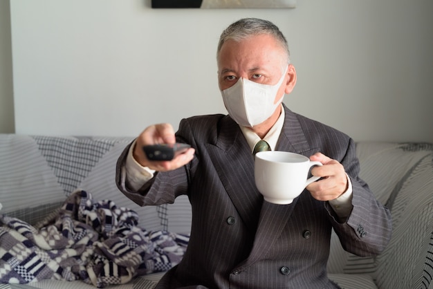 Uomo d'affari giapponese maturo con la maschera che resta a casa sotto la quarantena