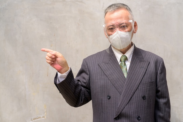 Uomo d'affari giapponese maturo con maschera e visiera che punta verso il lato