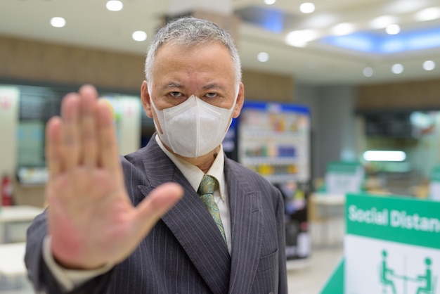 Uomo d'affari giapponese maturo sollecitato con il gesto di arresto di rappresentazione della maschera e l'allontanamento sociale alla corte di alimento