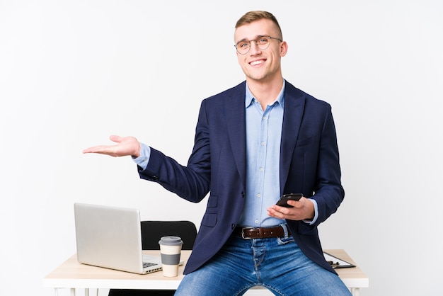 Uomo d'affari giovane con un computer portatile che mostra uno spazio di copia su un palmo e tenendo un'altra mano sulla vita.