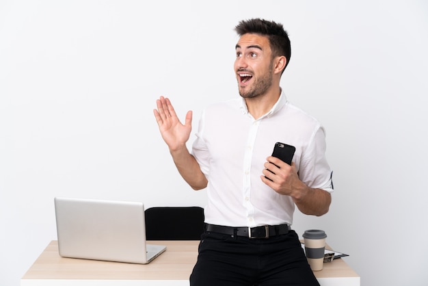 Uomo d'affari giovane con un telefono cellulare in un posto di lavoro con sorpresa espressione facciale