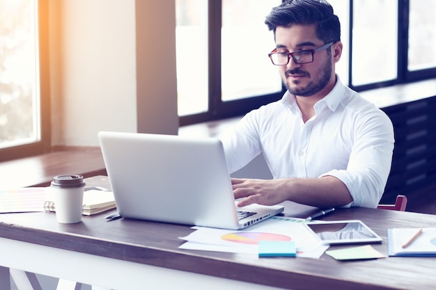 Uomo d'affari giovane hipster che lavora al computer portatile in ufficio moderno. Effetto pellicola, riflesso lente