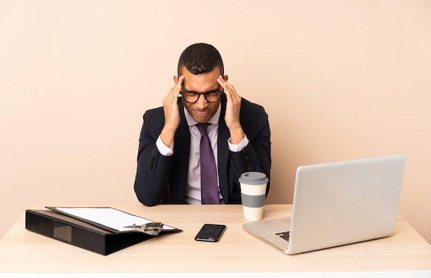Uomo d'affari giovane nel suo ufficio con un computer portatile e altri documenti con mal di testa