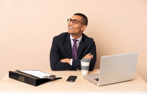 Uomo d'affari giovane nel suo ufficio con un computer portatile e altri documenti felici e sorridenti