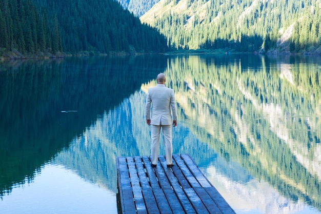 uomo d'affari in abito bianco è in piedi su un molo in riva al lago