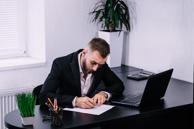 Uomo d'affari in abito scuro seduto alla scrivania dell'ufficio che firma un contra
