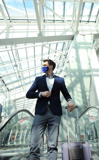 Uomo d'affari in maschera protettiva all'aeroporto che scende la scala mobile.