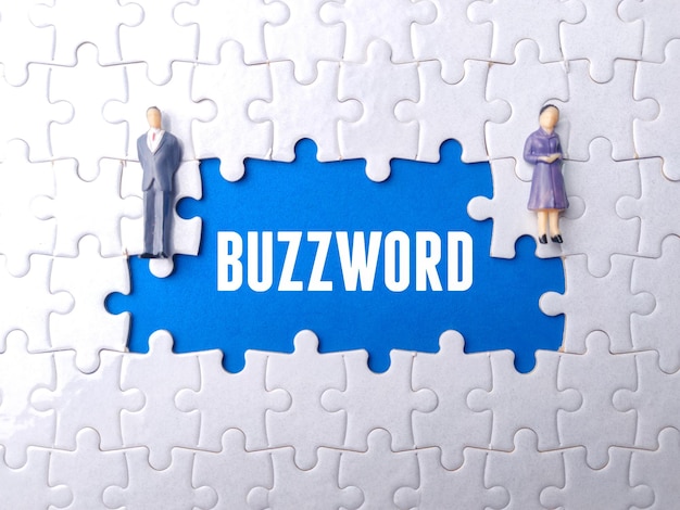 Uomo d'affari in miniatura e donne d'affari su un puzzle bianco con testo BUZZWORD