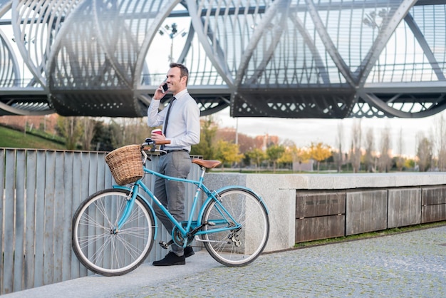 Uomo d'affari in piedi accanto alla sua bicicletta d'epoca che parla al telefono cellulare