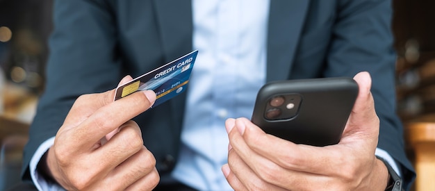 Uomo d'affari in tuta con carta di credito e utilizzo di smartphone touchscreen per lo shopping online mentre effettua ordini al bar o in ufficio. Business, tecnologia, e-commerce e concetto di pagamento online