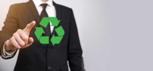Uomo d'affari in tuta su sfondo grigio tiene un'icona di riciclaggio, segno nelle sue mani. Ecologia, ambiente e concetto di conservazione
