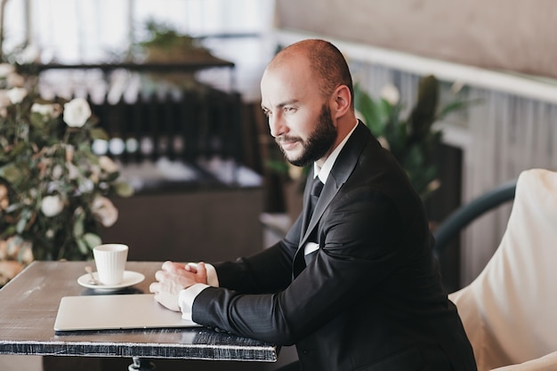 Uomo d'affari in un vestito costoso e guarda sedersi in un bar in attesa di un incontro