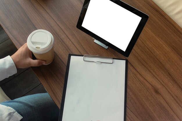 Uomo d'affari in una camicia bianca con una tavoletta digitale nelle sue mani firma un contratto in ufficio. Posto di lavoro con una tazza di caffè e un documento con una penna su un tavolo di legno.