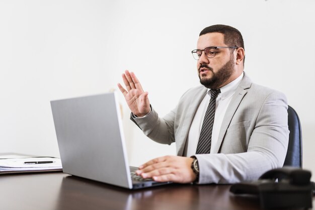 Uomo d'affari in una videoconferenza con laptop e documenti sulla sua scrivania, concetto di consulente avvocato.