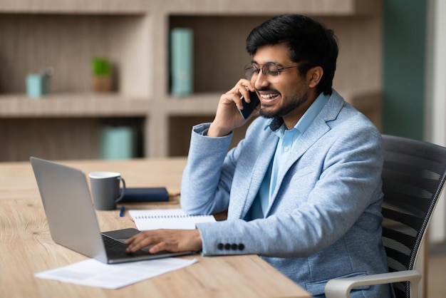 Uomo d'affari indiano impegnato in una conversazione telefonica usando un quaderno sul posto di lavoro