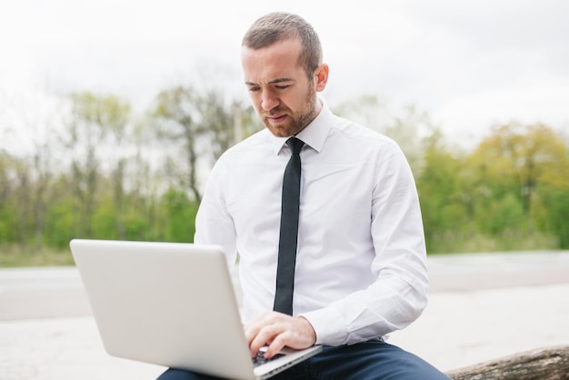 Uomo d'affari intelligente di moda che indossa una camicia bianca digitando sul suo computer che fa rapporto della sua azienda utilizzando wireless Bell'uomo che lavora su laptop all'aperto nel parco Tecnologia e concetto di business