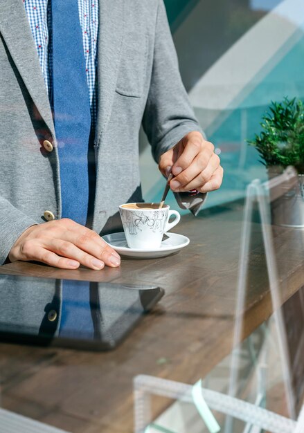 Uomo d'affari irriconoscibile che mescola il caffè in una caffetteria