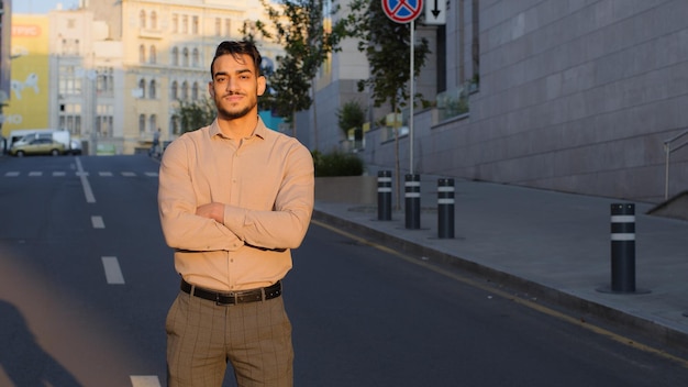 Uomo d'affari ispanico di successo ragazzo arabo si trova in città all'aperto sullo sfondo della strada con le braccia incrociate pensando pianificazione sognando con espressione seria meditando pensieri problema guai pensare