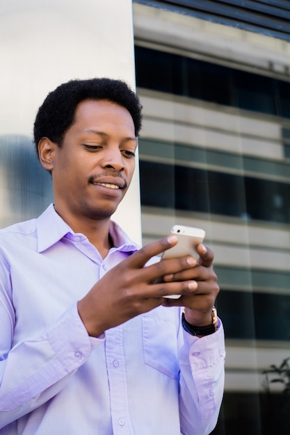 Uomo d&#39;affari latino che utilizza telefono cellulare nella città.