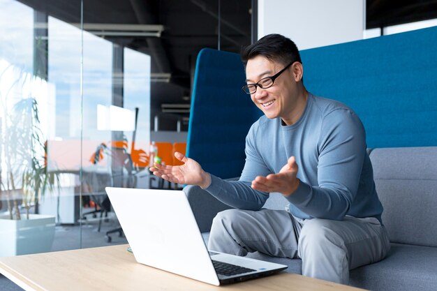 Uomo d'affari libero professionista felice e di successo che lavora dall'ufficio uomo asiatico divertendosi a parlare in videochiamata guardando la webcam