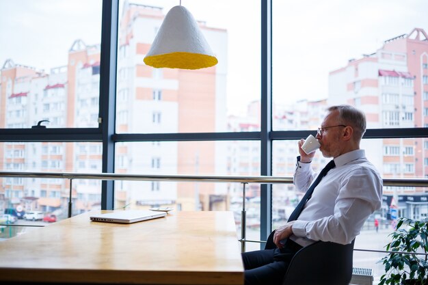 Uomo d'affari manager maschio adulto ha lavorato con successo e alla fine della giornata beve caffè senza giacca