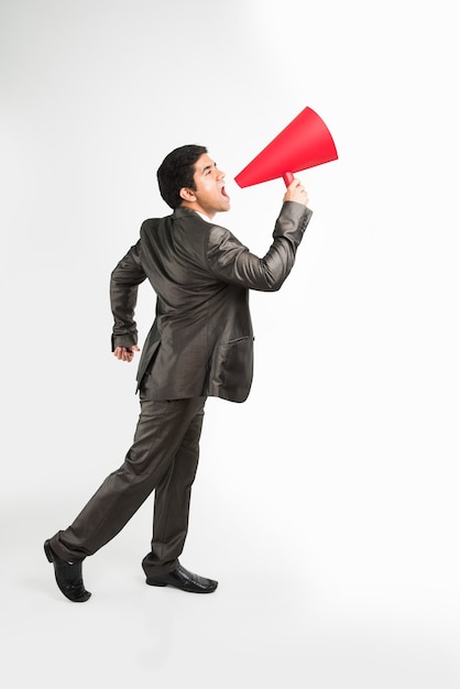 Uomo d'affari maschio asiatico indiano che annuncia o diffonde notizie utilizzando un altoparlante rosso o un mega microfono fatto di carta, isolato su sfondo bianco