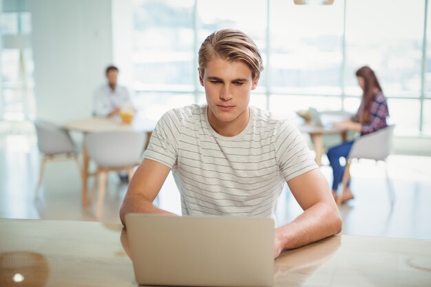 Uomo d'affari maschio che si siede sullo scrittorio e che per mezzo del computer portatile