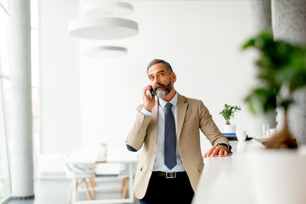 Uomo d&#39;affari maturo bello con il telefono cellulare nell&#39;ufficio