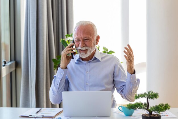 Uomo d'affari maturo che lavora al computer portatile e che parla sul cellulare Leader di affari maturo bello che si siede in un ufficio moderno