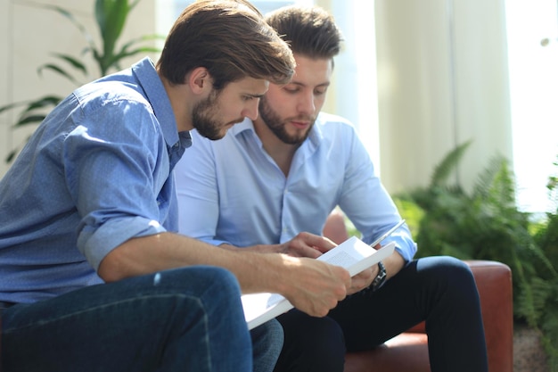 Uomo d'affari maturo che utilizza una tavoletta digitale per discutere le informazioni con un collega più giovane in un moderno ufficio commerciale